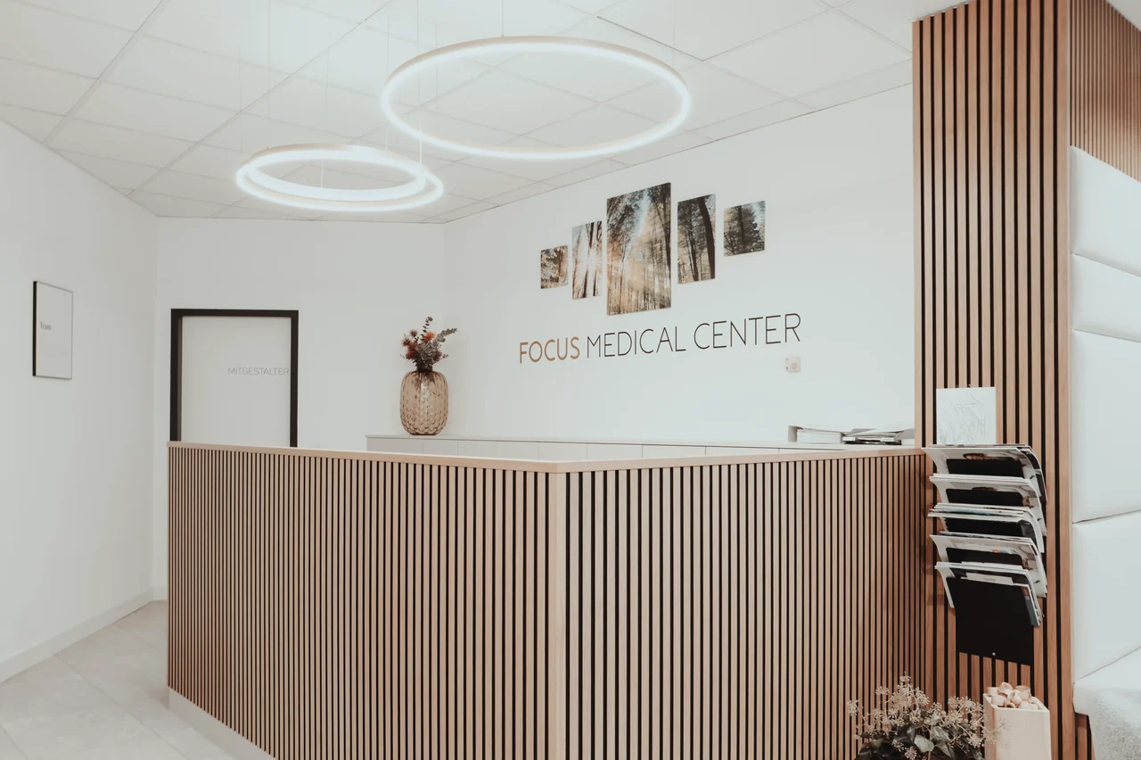 Leerer Empfangstresen aus Holzlamellen mit Wandschriftzug Focus Medical und Deko-Vase.