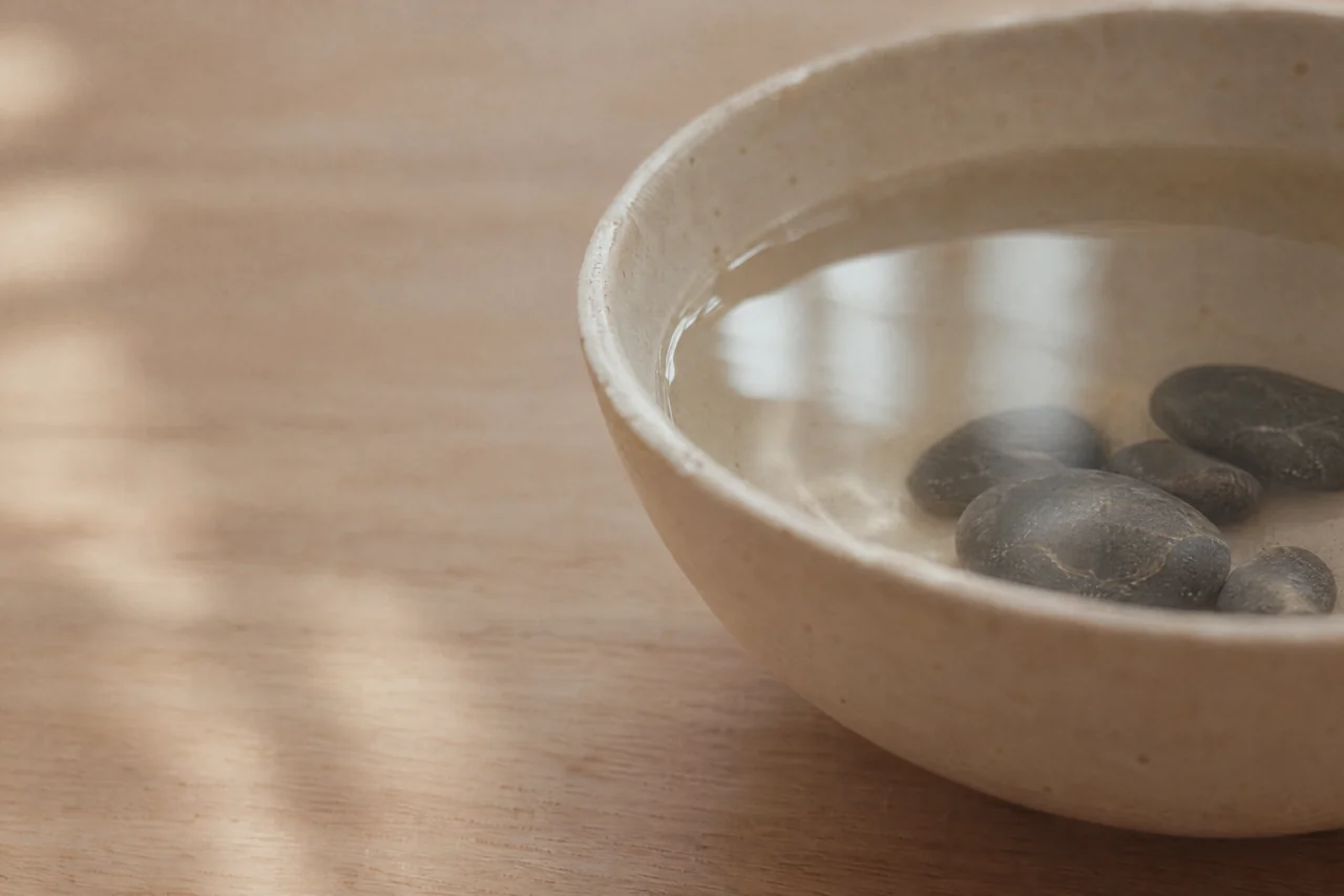Dunkle Kiesel in einer hellen Keramikschale mit klarem Wasser.