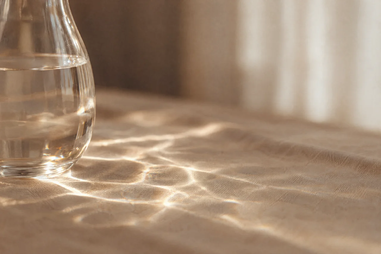Eine Glaskaraffe mit Wasser, deren Licht ein Muster auf Leinen zeichnet.