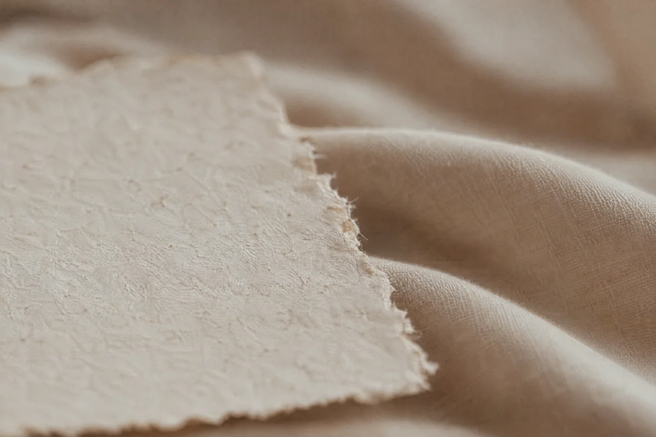 Raues handgeschöpftes Papier auf glattem Leinen im Streiflicht.