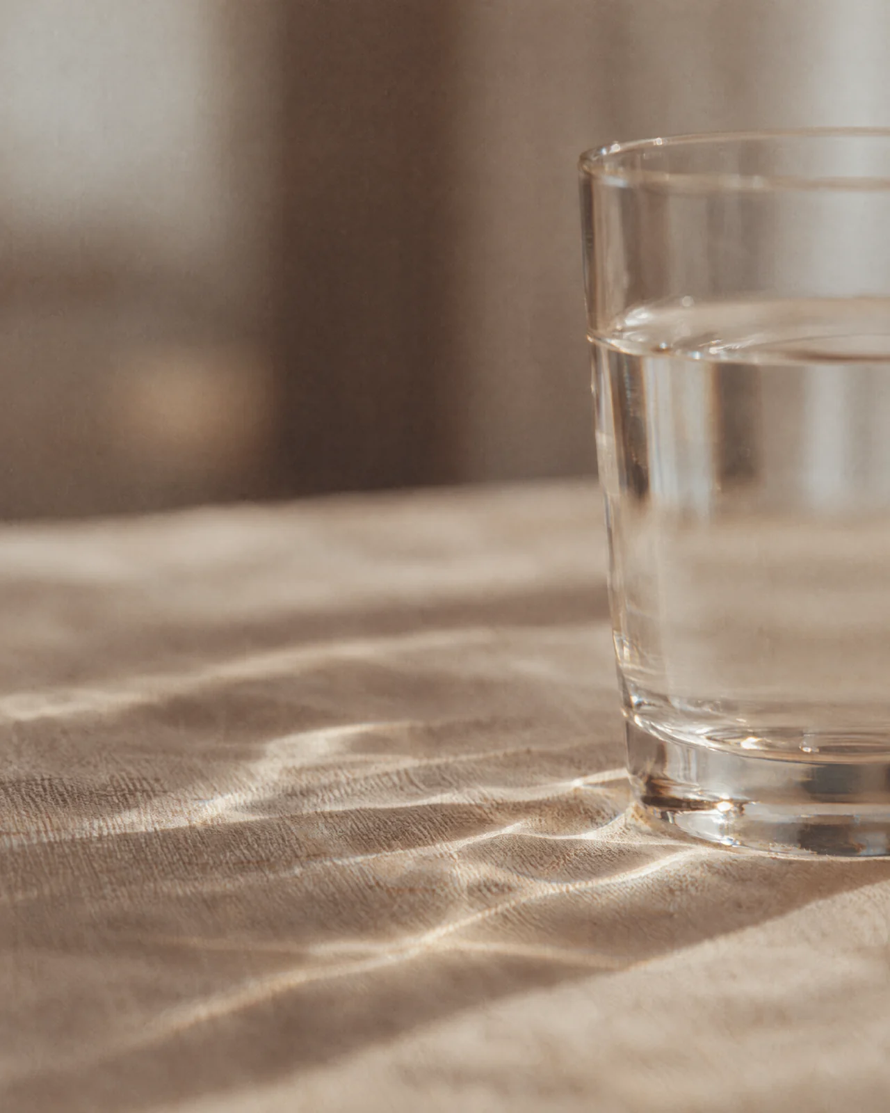 Ein Glas Wasser wirft Lichtmuster auf hellen Leinenstoff.